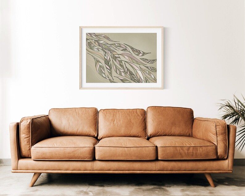 May include: A framed abstract art print with a green and brown color scheme. The print features a stylized design of leaves and branches. The print is hanging on a white wall above a brown leather sofa.