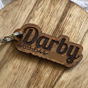 May include: Wooden pet tag with the name "Darby" and phone number "469-644" engraved on it. The tag is attached to a silver key ring.