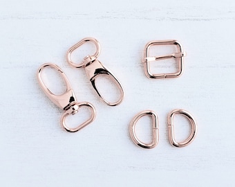 May include: A set of five rose gold metal hardware pieces for crafting. The set includes two swivel clasps, two D-rings, and a rectangular buckle.