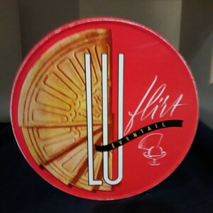 Peut inclure: Une boîte ronde rouge avec une image dorée et blanche d'un biscuit gaufré. Le texte "LU" est en blanc et le texte "flirt éventail" est en noir.