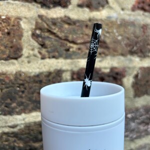 Puede incluir: Una taza de viaje blanca con un dise&ntilde;o de telara&ntilde;a negra y una pajita con estampado de telara&ntilde;a negra y blanca.