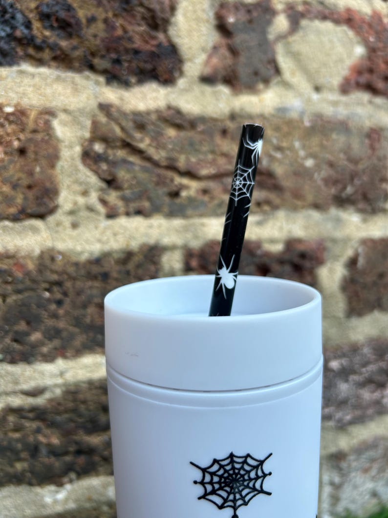 Puede incluir: Una taza de viaje blanca con un dise&ntilde;o de telara&ntilde;a negra y una pajita con estampado de telara&ntilde;a negra y blanca.