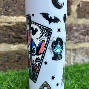 Puede incluir: Un vaso blanco con una variedad de pegatinas en blanco y negro. Las pegatinas incluyen una luna creciente, un murci&eacute;lago, una bola de cristal, una carta de tarot con un personaje de dibujos animados azul y rosa, y una tabla de Ouija negra y dorada con el texto "GOODBYE".