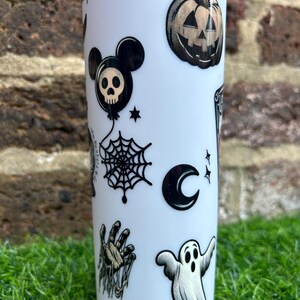 Puede incluir: Vaso blanco con pegatinas de tem&aacute;tica de Halloween en negro y dorado. Las pegatinas incluyen un fantasma, una telara&ntilde;a, un murci&eacute;lago, una calabaza, una calavera, una mano, una luna creciente y una cabeza de Mickey Mouse con una calavera en su interior.