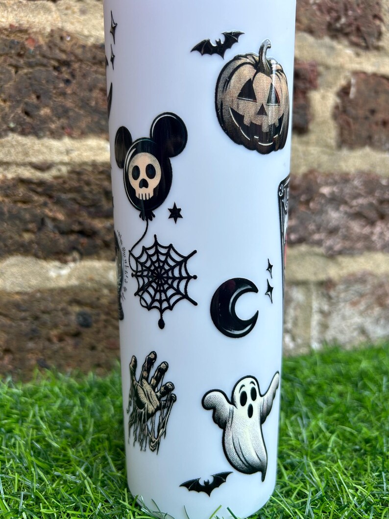Puede incluir: Vaso blanco con pegatinas de tem&aacute;tica de Halloween en negro y dorado. Las pegatinas incluyen un fantasma, una telara&ntilde;a, un murci&eacute;lago, una calabaza, una calavera, una mano, una luna creciente y una cabeza de Mickey Mouse con una calavera en su interior.