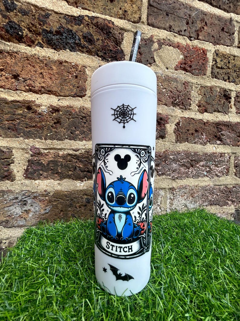 Puede incluir: Un vaso blanco con una ilustraci&oacute;n en blanco y negro de Stitch de Lilo & Stitch. La ilustraci&oacute;n es de estilo vintage con una telara&ntilde;a, un murci&eacute;lago y el texto "Stitch".