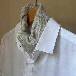 May include: A white dress shirt with a grey scarf tied around the collar.