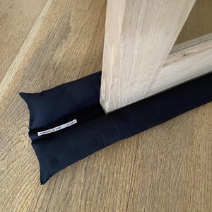 May include: Black door draught stopper with a white label that reads "Scandalo of Sole - London".