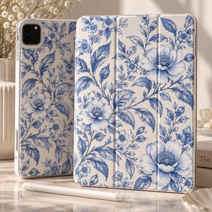 Könnte beinhalten: Eine Tablet-Hülle und eine passende Smartphone-Hülle, beide mit weißem Hintergrund und einem blauen Blumenmuster aus blühenden Blüten und Blättern. Ein weißer Eingabestift liegt horizontal vor den Hüllen.