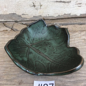 May include: A dark green ceramic leaf-shaped dish with a raised vein pattern. The dish is sitting on a wooden surface. #87