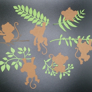 Puede incluir: Seis recortes de papel marrón de monos columpiándose de recortes de papel verde de ramas. Los monos están en varias poses, algunos se agarran a las ramas con las manos, mientras que otros se balancean por las colas.