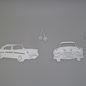 Puede incluir: Un conjunto de formas met&aacute;licas troqueladas de color plateado que incluyen dos coches cl&aacute;sicos, un par de dados colgantes y dos se&ntilde;ales de flecha. Las formas son planas con contornos y detalles en relieve sobre un fondo gris s&oacute;lido.
