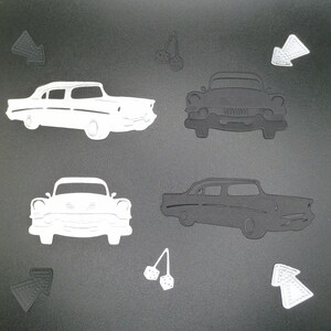 Puede incluir: Una colecci&oacute;n de formas troqueladas que incluye dos siluetas de coches cl&aacute;sicos en blanco y dos en negro, dos flechas en blanco y dos en negro, y dos pares de dados colgantes en blanco y negro sobre una superficie gris oscuro.