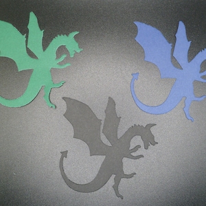 May include: Three paper dragon cutouts in different colors: green, blue, and black. The dragons are three-headed and have wings.