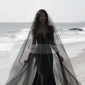 May include: A floor-length black veil made of sheer, lightweight tulle fabric. The veil features a soft, flowing drape that extends outwards from the head. A semi-transparent oval overlay with the text Camille Vesper studio is centred on the image.