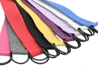 Könnte beinhalten: Ein Satz von acht bunten Stoffbändern mit schwarzen Metallringen an den Enden. Die Bänder sind fächerförmig angeordnet, wobei das rosa Band unten und das blaue Band oben liegt.