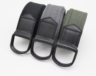 Könnte beinhalten: Drei Canvas-Gürtel in Schwarz, Grau und Olivgrün. Jeder Gürtel hat einen schwarzen Lederakzent und eine Metallschnalle mit D-Ring. Die Gürtel werden auf weißem Hintergrund präsentiert.