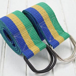 Può includere: Due cinture a righe con anelli a D. Una cintura ha un anello a D nero, l'altra argentato. Le cinture hanno strisce blu, verdi e gialle. Le cinture sono realizzate in materiale tessuto.
