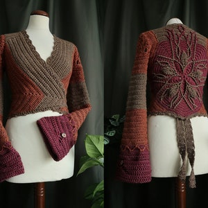 May include: A crocheted wrap cardigan with long sleeves and a tie closure. The cardigan is made in a brown, orange, and burgundy color scheme. The back of the cardigan features a large crocheted flower design.