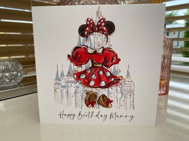 K&ouml;nnte beinhalten: Eine Gru&szlig;karte mit einer Cartoon-Illustration von Minnie Mouse in einem rot-wei&szlig; gepunkteten Kleid, die vor dem Schloss von Aschenputtel steht. Die Karte tr&auml;gt den Text "Happy Birthday Mummy".