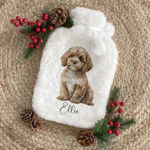 May include: A white faux fur hot water bottle cover featuring a printed illustration of a brown curly-haired puppy sitting down. The name Ellie is printed in black script below the puppy. The cover includes a white ribbon tie at the top.