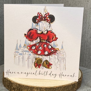 K&ouml;nnte beinhalten: Eine wei&szlig;e Karte mit einer roten und schwarzen Illustration einer Comicfigur vor einem blauen und wei&szlig;en Schloss. Der Text "Have a magical birthday Hannah" ist auf der Karte gedruckt.
