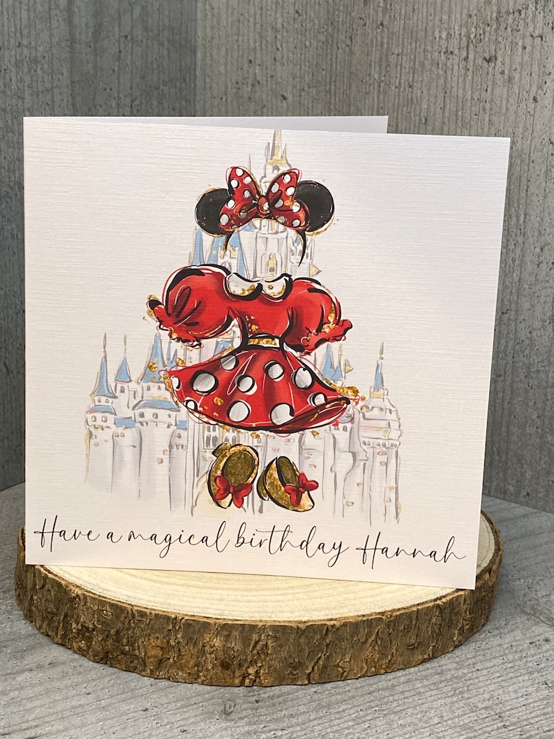K&ouml;nnte beinhalten: Eine wei&szlig;e Karte mit einer roten und schwarzen Illustration einer Comicfigur vor einem blauen und wei&szlig;en Schloss. Der Text "Have a magical birthday Hannah" ist auf der Karte gedruckt.