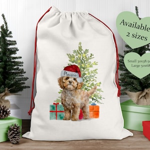 May include: White Christmas sack with a red drawstring. The sack features a watercolour illustration of a dog wearing a Santa hat, standing in front of a Christmas tree with presents. The dog's name is "Maisie". Available in two sizes: small (30x38.5cm) and large (50x68cm).