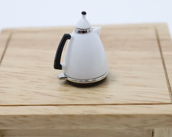Op de afbeelding: Een miniatuur wit elektrisch waterkoker met een zwarte handgreep staat op een houten tafel.