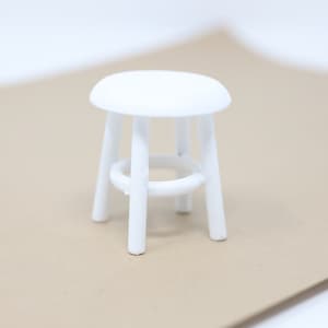 May include: A white wooden stool with a round seat and four legs. The stool is made of simple, clean lines and is perfect for a minimalist decor.