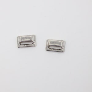 May include: Two silver metal rectangular-shaped clasps with a small opening in the centre.