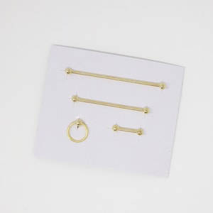 May include: A set of three gold barbell body jewelry pieces with ball ends and one gold ring with a ball end. The jewelry is displayed on a white card.