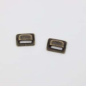 May include: Two antique gold-toned metal slider buckles. Each buckle is rectangular in shape with a rounded top and a small opening in the centre.