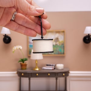 May include: A miniature black and white pendant light fixture with a white fabric shade and black trim. The light is hanging from a black chain.