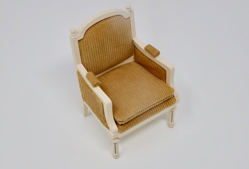 Puede incluir: Un peque&ntilde;o sill&oacute;n de madera blanco con un coj&iacute;n de terciopelo marr&oacute;n. El sill&oacute;n tiene un respaldo curvo y un dise&ntilde;o sencillo.