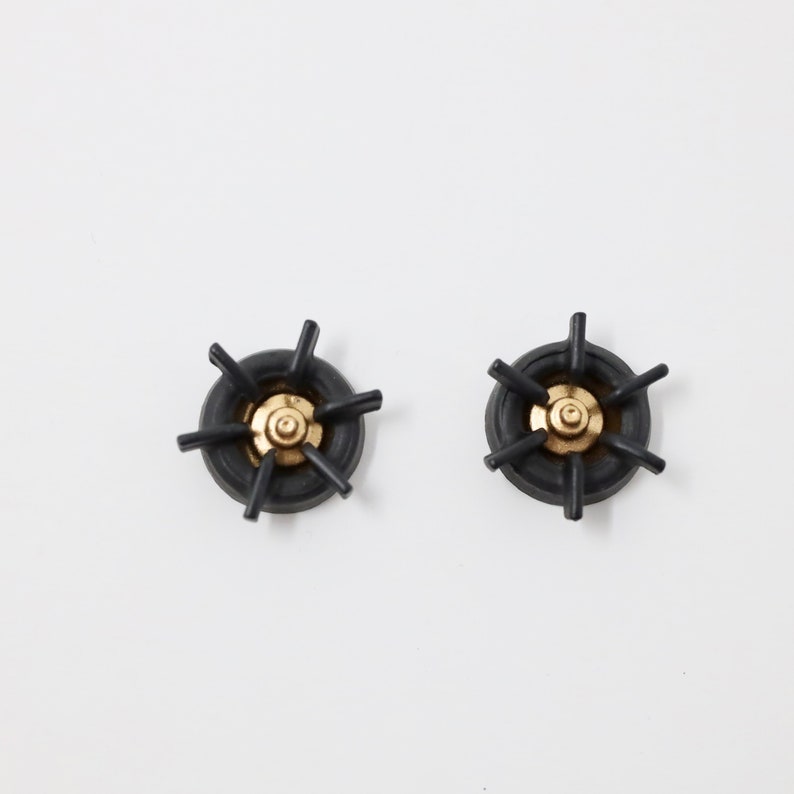 K&ouml;nnte beinhalten: Zwei schwarze Metall-Kochfeld-Roste mit goldenen Mittelpunkten.