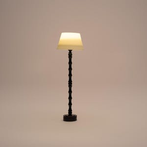 Op de afbeelding: Een zwarte staande lamp met een witte lampenkap van stof. De lamp heeft een hoge, slanke voet met een reeks decoratieve ringen.