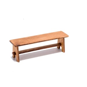 Peut inclure: Un banc en bois au design simple, avec un dessus plat et une seule poutre de soutien en dessous. Le banc est en bois naturel avec une finition brun clair.