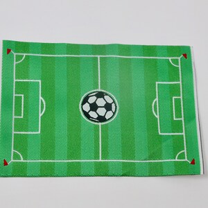 May include: A green felt soccer field with white lines and a black and white soccer ball in the center. The field has red corner flags.