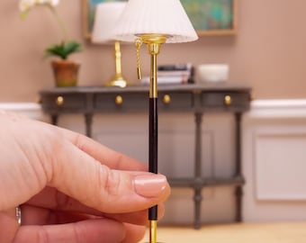 May include: A gold and black floor lamp with a white pleated lampshade. The lamp has a pull chain and a round base.