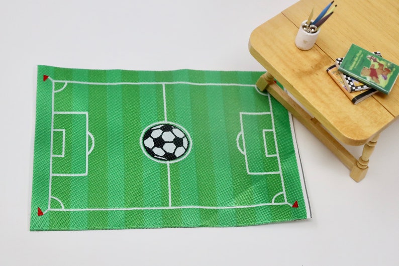 May include: Green and white soccer field rug with a black and white soccer ball in the center. The rug has white lines marking the field and goal areas.