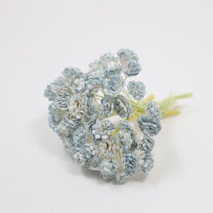 May include: A bunch of light blue paper flowers with white centers. The flowers are arranged in a cluster and have a delicate, airy appearance.