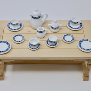 May include: A miniature porcelain tea set with blue and white geometric patterns. The set includes a teapot, creamer, sugar bowl, four cups, and four saucers. The set is displayed on a wooden table.