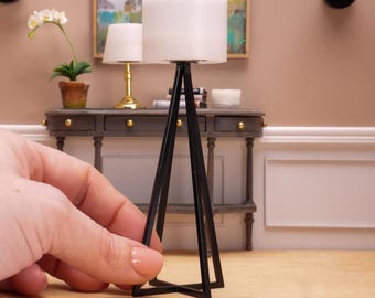 May include: A black tripod floor lamp with a white drum shade. The lamp is on a wooden surface in front of a console table.