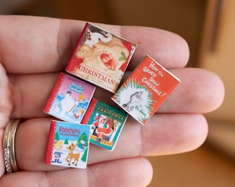 Op de afbeelding: Vijf miniatuurboeken met kerstthema met geïllustreerde covers getiteld The Night Before Christmas, How The Grinch Stole Christmas, Frosty the Snowman, Rudolph the Red-Nosed Reindeer en een tweede versie van The Night Before Christmas.
