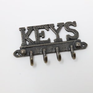 May include: A black metal key holder with the word "KEYS" in raised letters and five hooks.