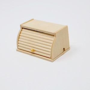 May include: A wooden bread box with a roll-top lid and a small yellow knob. The box is made of light wood and has a natural finish.