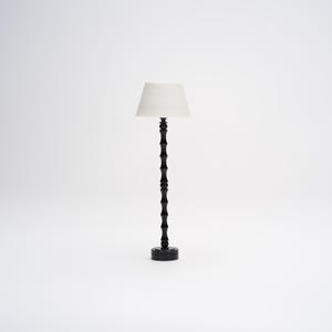Op de afbeelding: Een zwarte staande lamp met een witte lampenkap. De lamp heeft een uniek ontwerp met een reeks ronde knoppen op de basis en de steel.
