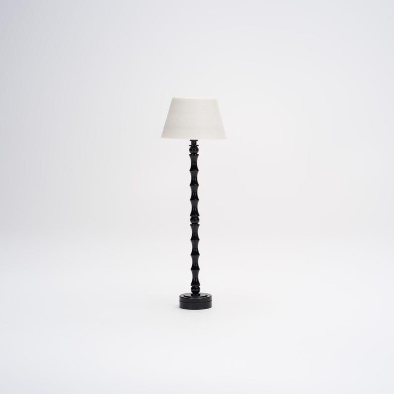 Op de afbeelding: Een zwarte staande lamp met een witte lampenkap. De lamp heeft een uniek ontwerp met een reeks ronde knoppen op de basis en de steel.