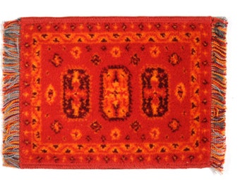 May include: A red, orange, and black patterned rug with fringe on all sides. The rug has a geometric design with a central motif of three stylized ovals.